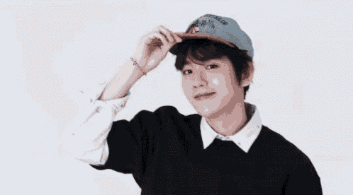a young man wearing a baseball cap and a black sweater is standing in front of a white background .