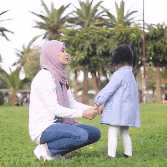 a woman in a hijab holds the hand of a little girl in a blue dress