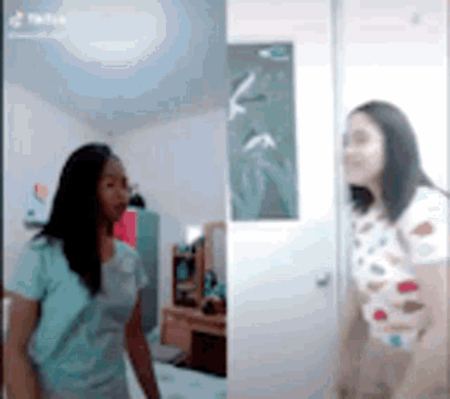 two women are standing next to each other in a bedroom and looking at each other .