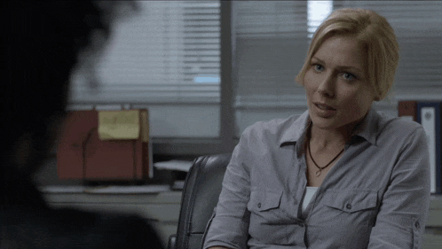 a woman in a grey shirt sits in a chair talking to another person