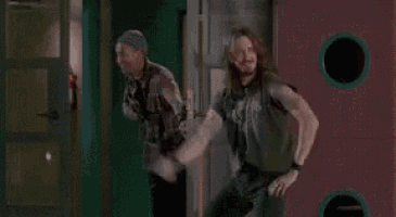 a man with long hair is dancing in a hallway while another man stands behind him .