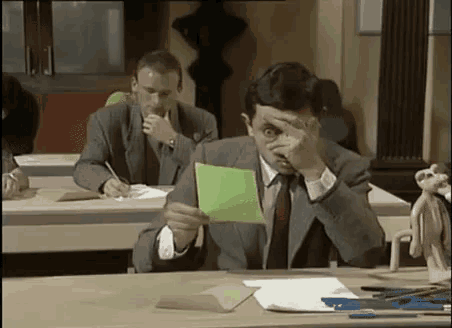 a man in a suit and tie is sitting at a desk holding a green piece of paper .