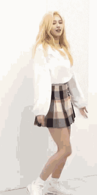 a woman wearing a plaid skirt and a white crop top is dancing in a room .