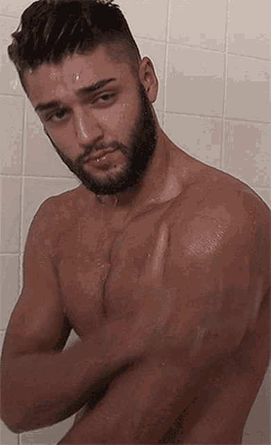 a shirtless man with a beard is taking a shower in a bathroom