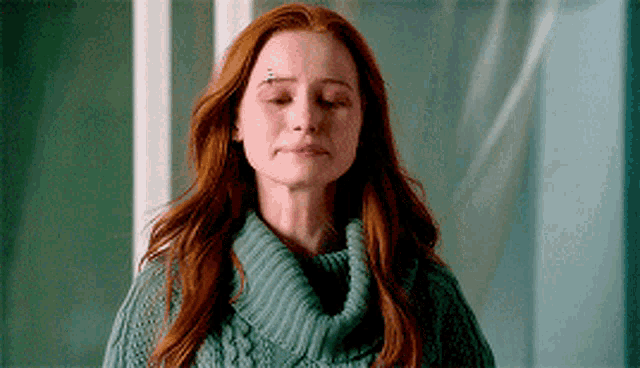 a woman with red hair is wearing a green sweater with her eyes closed and a tattoo on her forehead .