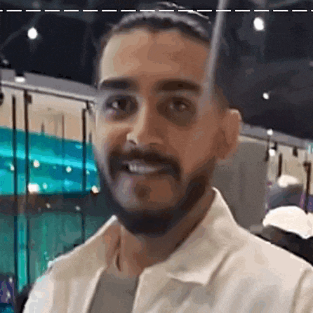 a man with a beard is smiling and looking at the camera while wearing a white jacket .