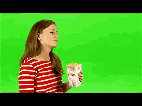 a woman in a striped shirt is eating popcorn on a green screen