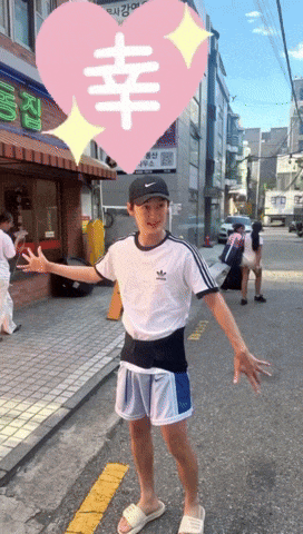 a boy wearing a white adidas shirt is standing on a street
