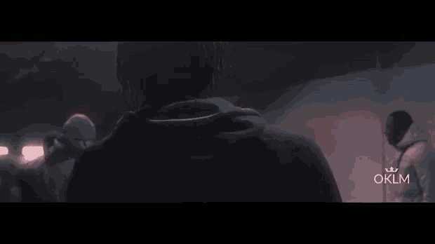 a man in a dark room with oklm written on the bottom right corner