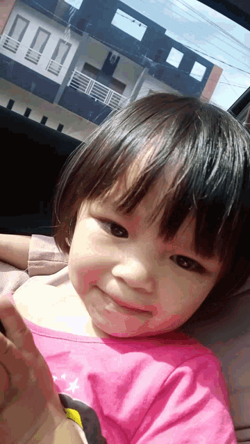 a little girl in a pink shirt is sitting in the back seat of a car
