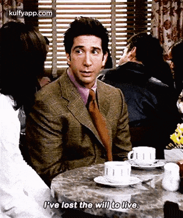 a man in a suit and tie is sitting at a table with a cup of coffee and a plate of food .