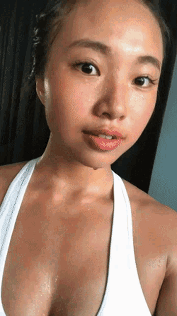 a woman wearing a white tank top has sweat on her face