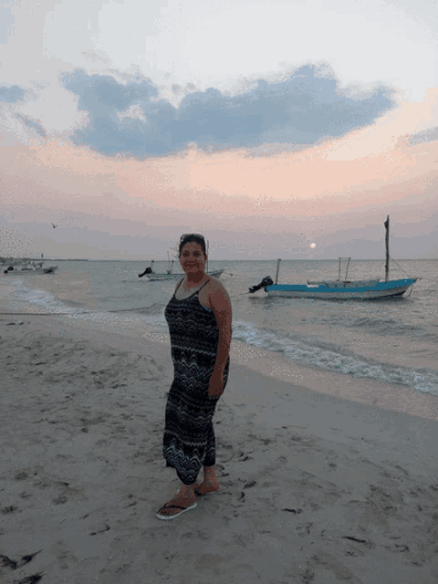 a woman in a black and white dress stands on a beach with boats in the background