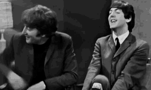 two men in suits and ties are sitting next to each other in a room .