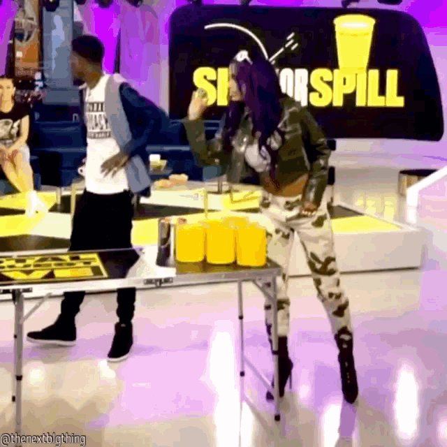 a man and a woman are playing beer pong in front of a sign that says show spill