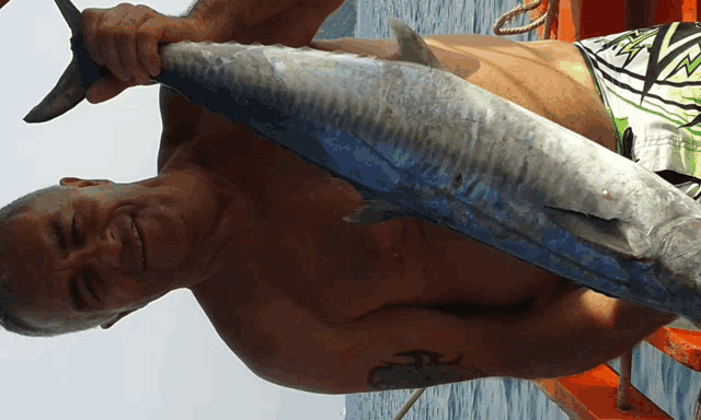 a shirtless man is holding a large fish in his hand