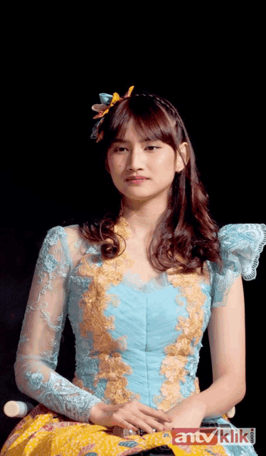 a woman in a blue and gold dress is sitting in front of a black background