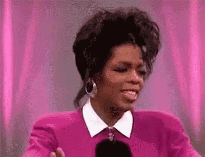 oprah winfrey is wearing a pink sweater and a white collar and smiling .