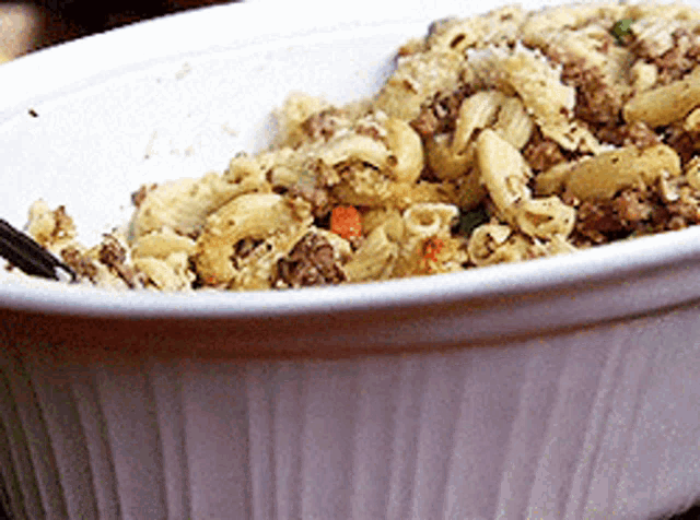 a white bowl filled with macaroni and meat with chopsticks