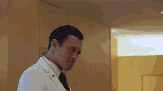 a man in a white coat and black tie stands in a room
