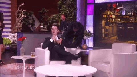 a man in a suit sits in a chair on a show sponsored by ellentube