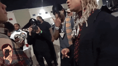 a group of people are standing around a man with dreadlocks smoking a cigarette