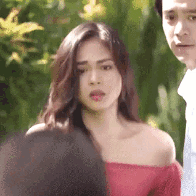 a man and a woman are standing next to each other and the woman is wearing a red off the shoulder top .