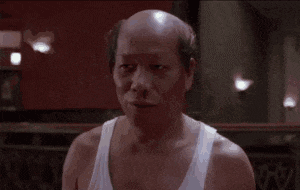 a bald man wearing a white tank top is standing in a dark room .