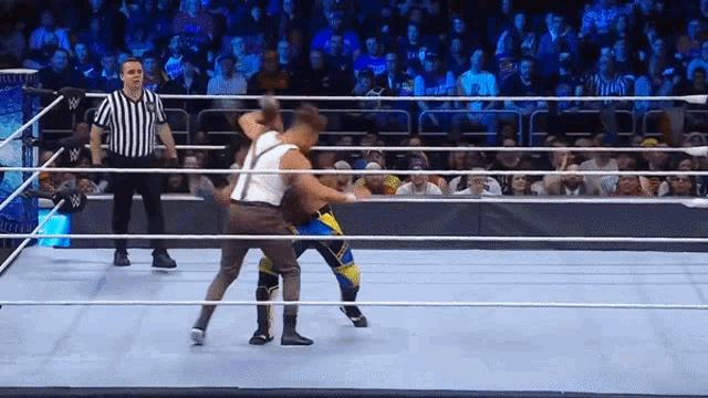 a referee watches two men wrestle in a ring