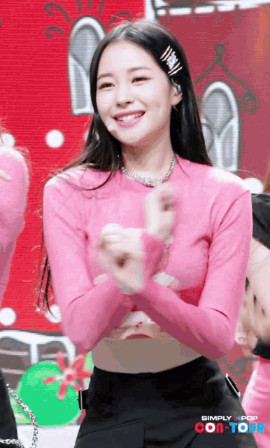 a woman in a pink sweater is smiling in front of simply pop con-tour
