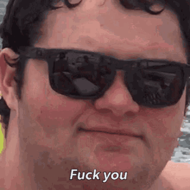 a man wearing sunglasses is making a funny face and saying fuck you .