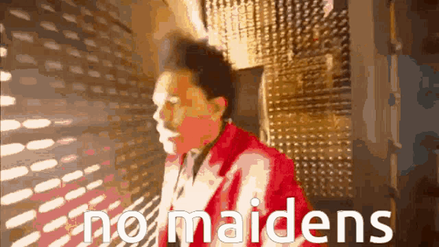 a man in a red jacket is standing in front of a wall with the words no maidens on it