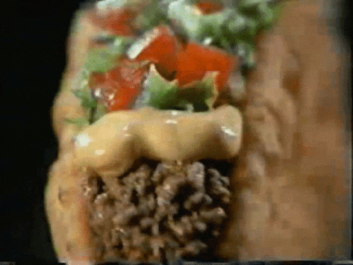 a close up of a taco with cheese lettuce and tomatoes on a black background