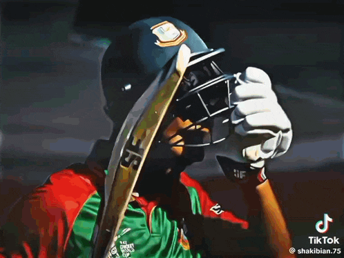 a man in a green and red shirt is holding a cricket bat over his head .