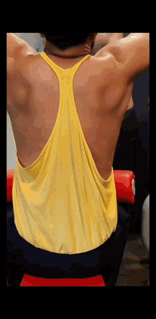 a man in a yellow tank top is sitting on a bench