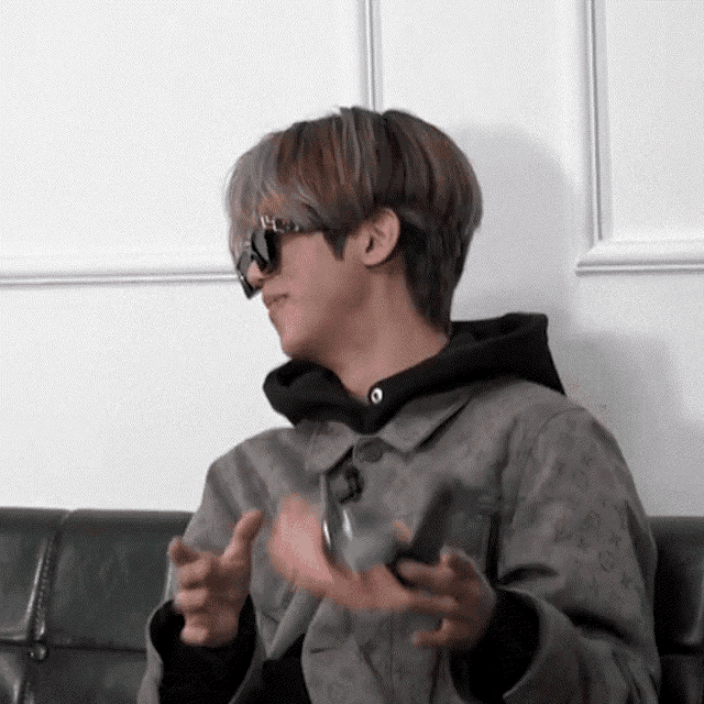 a man wearing sunglasses and a grey jacket is sitting on a couch