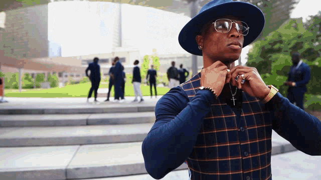 a man wearing a hat and sunglasses is adjusting his shirt