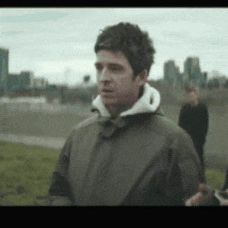 a man wearing a green jacket and a white hoodie is standing in a field .