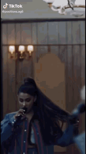 ariana grande is singing into a microphone in a room with a mirror .