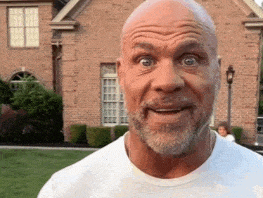 a bald man with a beard making a funny face in front of a brick house