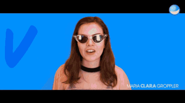 a woman wearing sunglasses and a choker stands in front of a pink background with the letters va and maria clara gropper