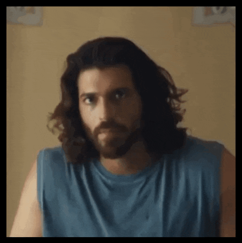 a man with long hair and a beard wearing a blue tank top .