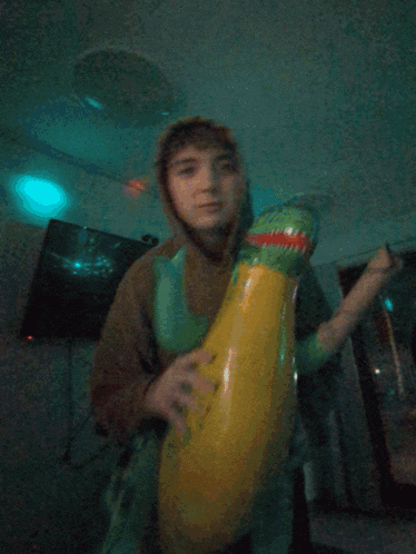 a man in a hoodie holds a large inflatable frog