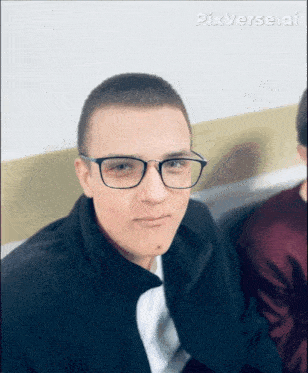 a young man wearing glasses and a black jacket looks at the camera
