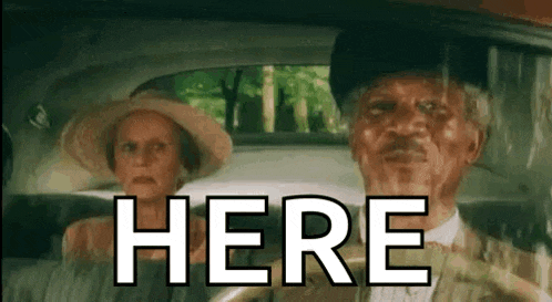 a man and a woman are sitting in a car with the word here written on the screen .