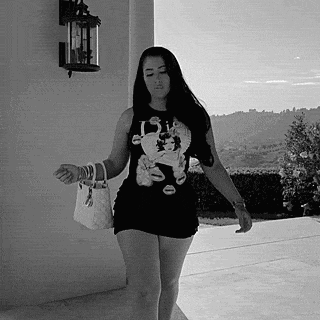 a woman in a black dress is walking down a sidewalk holding a white bag .