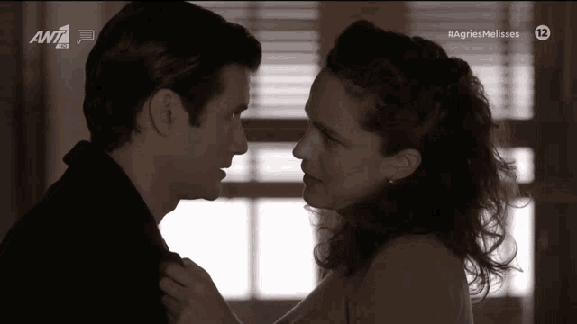 a man and a woman are looking at each other in a black and white photo with the ant1 logo behind them