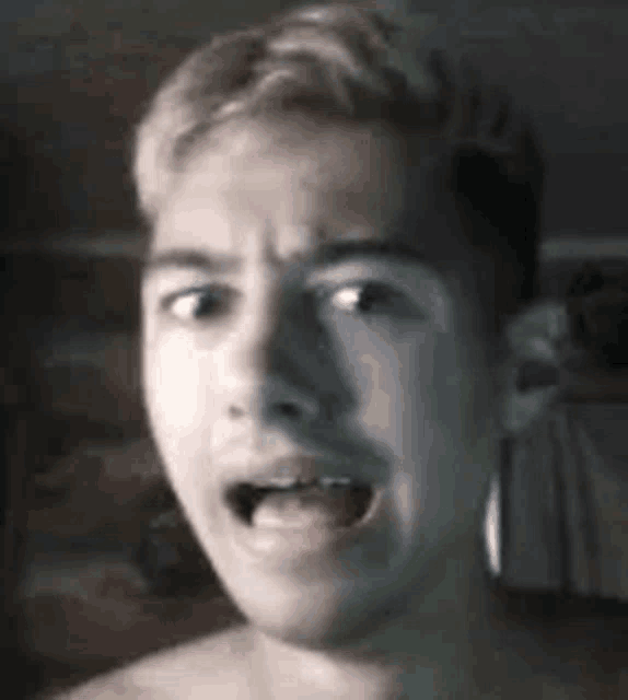 a shirtless young man is making a funny face with his mouth open in a dark room .