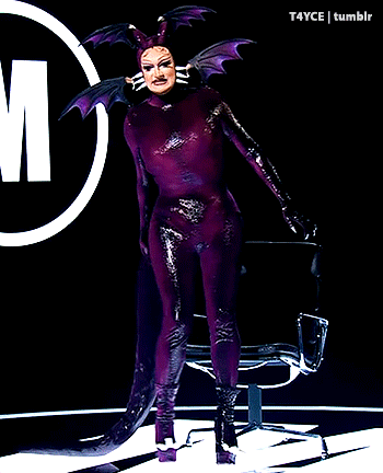 a woman in a purple costume is standing in front of a circle with the letter m in it
