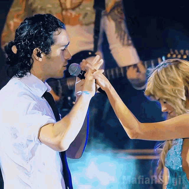a man holding a woman 's hand in front of a microphone with the word mafia on the bottom right